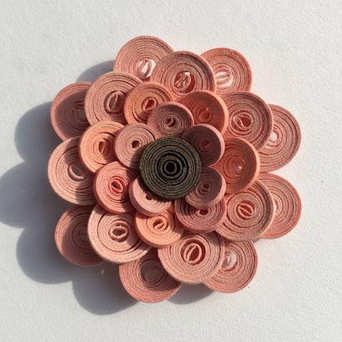 Colorful paper quilling coils in pink, coral, and gold arranged into a delicate flower shape showing visible spiral texture and dimensionality