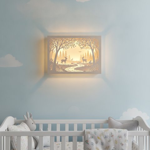 A finished illuminated layered papercut woodland shadow box mounted on a pastel nursery wall glowing with warm LED light