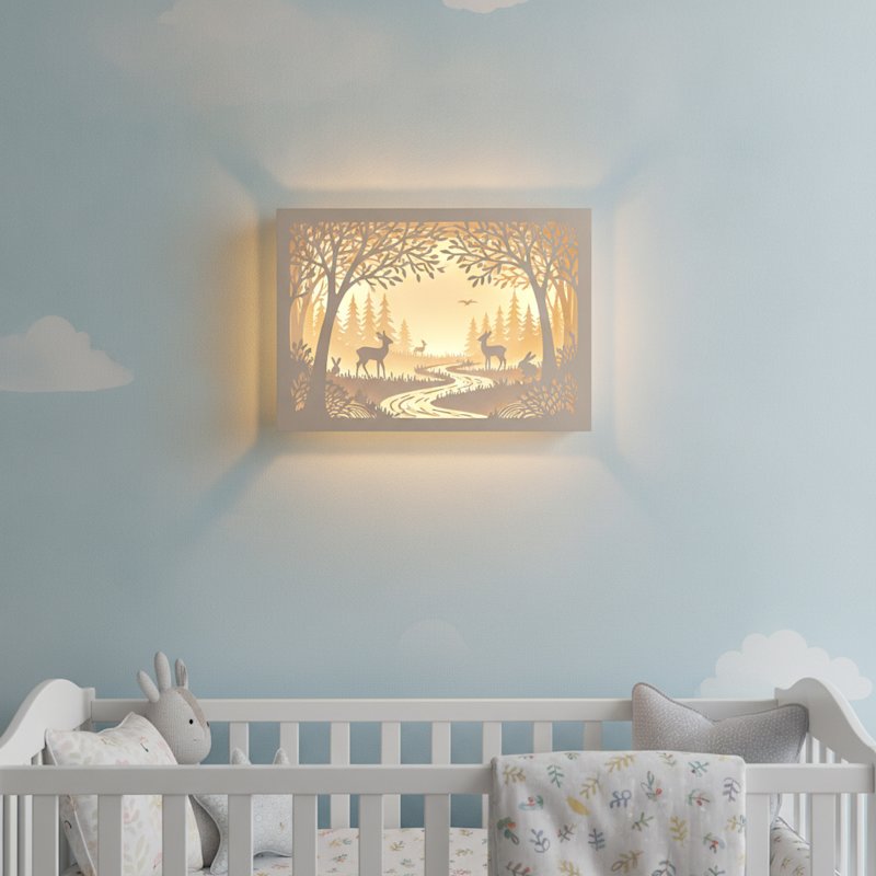 A finished illuminated layered papercut woodland shadow box mounted on a pastel nursery wall glowing with warm LED light